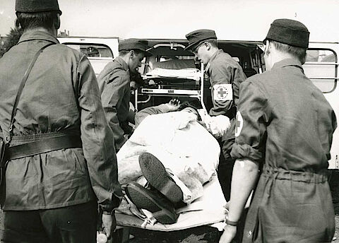 Rettungseinsatz bei einem Unfall: Sanitäter tragen einen Verletzten in einen Krankenwagen, sechziger Jahre 