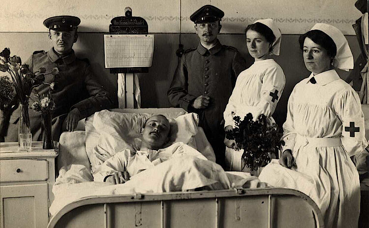 Krankenschwestern und Soldaten am Krankenbett eines Verwundeten (DRK)