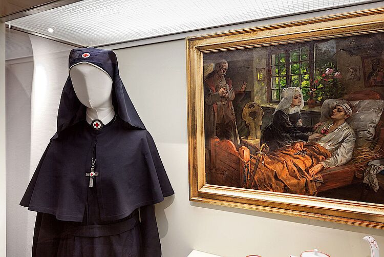 Festtagstracht der Badischen Luisenschwestern in der Rotkreuz-Museum Luckenwalde, dazu zeitgenössische Szene an einem Sterbebett (Jörg F. Müller / DRK)